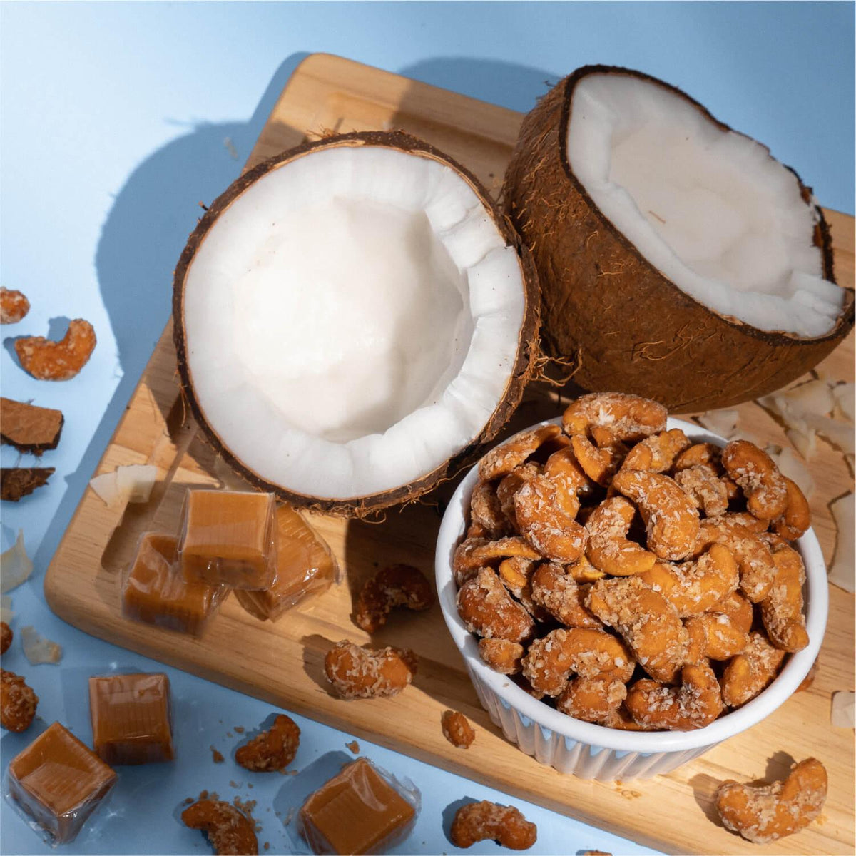 Bowl of coconut caramel cashews beside halved coconuts and caramels