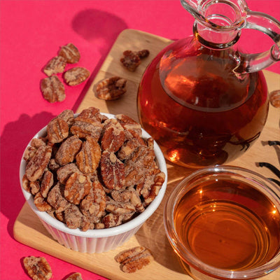 Bowl of maple cinnamon candied pecans beside a jar of maple syrup