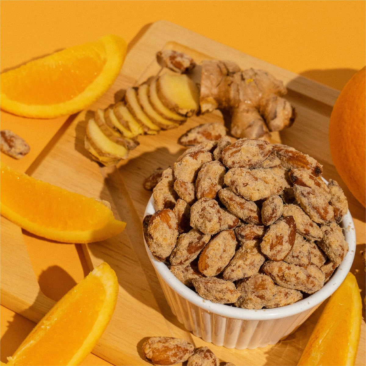 Bowl of orange ginger almonds with orange slices and fresh ginger